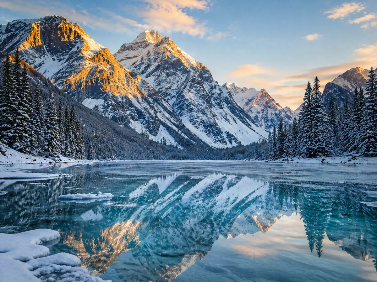 Lago helado en Banff con reflejo de montañas nevadas de las Rocosas canadienses al atardecer
