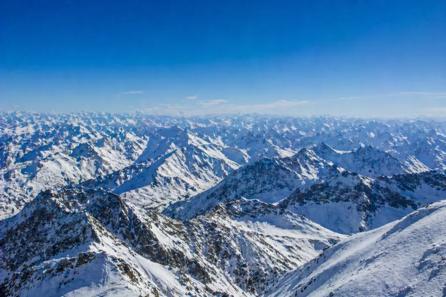 Panorámica aérea de cordilleras nevadas infinitas con cielo azul profundo