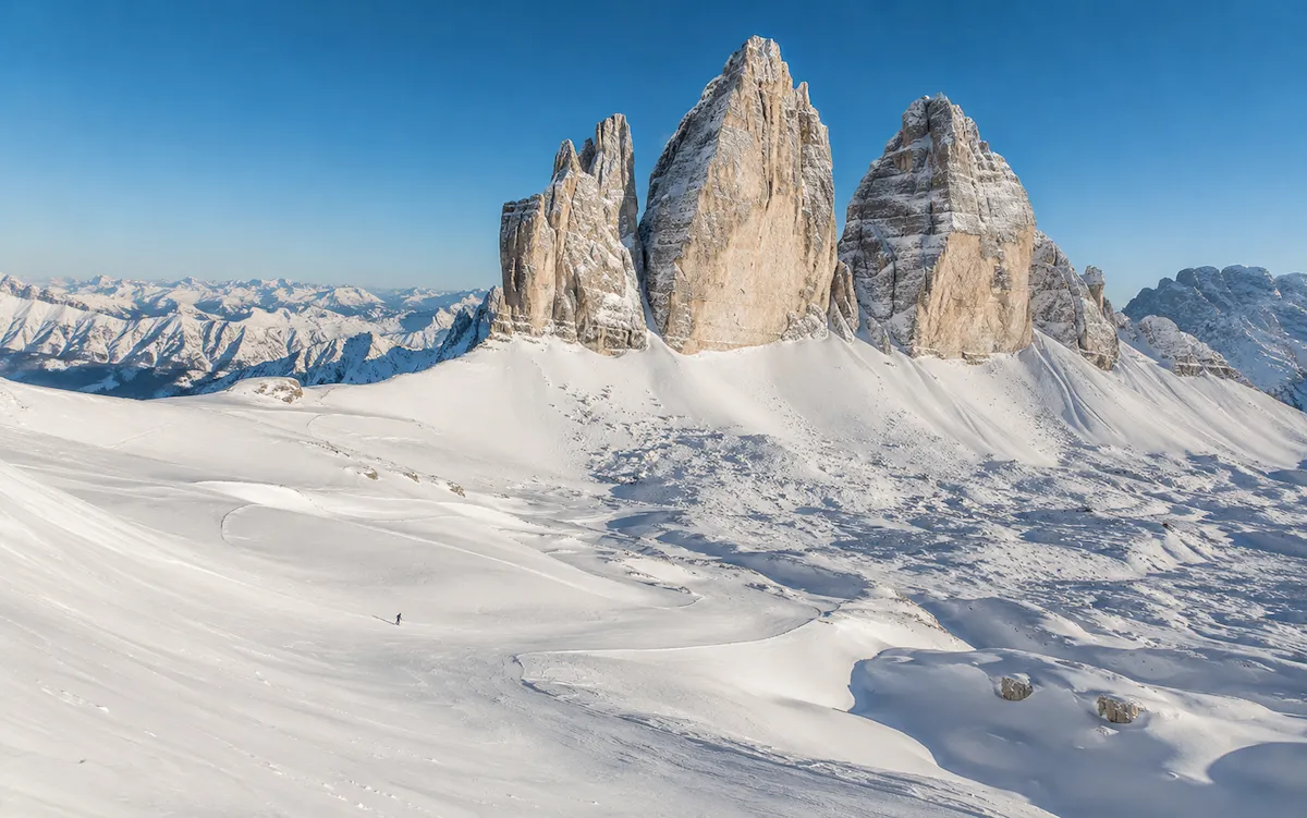 Tre Cime di Lavaredo en invierno, con un esquiador atravesando el paisaje nevado de 3 Zinnen Dolomites.