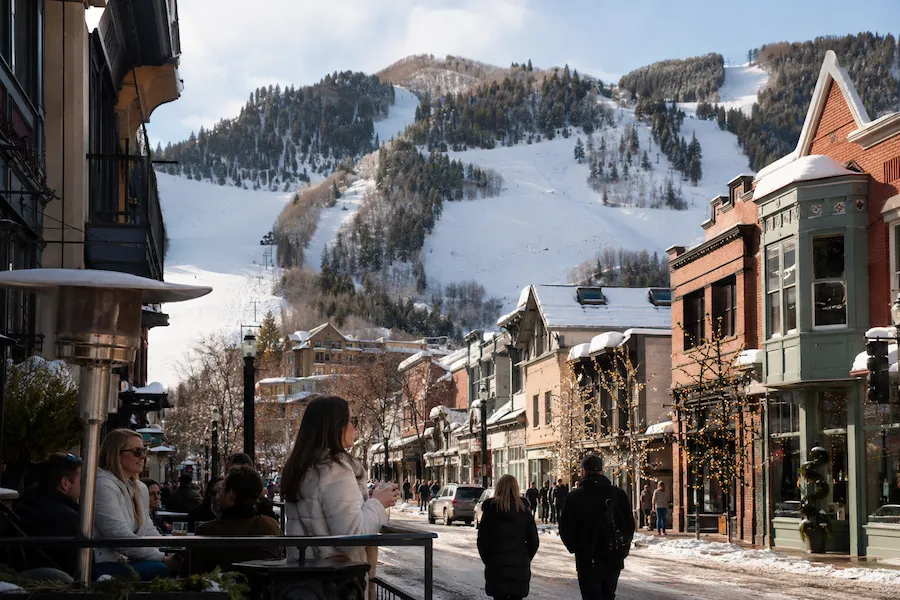 Calle nevada de Aspen con boutiques, terrazas y la montaña de esquí al fondo