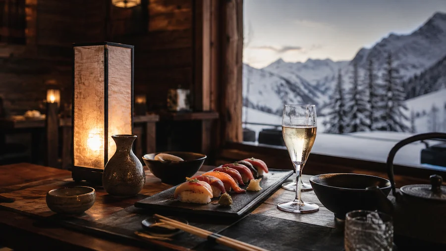 Mesa de estilo japonés con sushi, sake y vajilla cerámica frente a una ventana con montañas nevadas