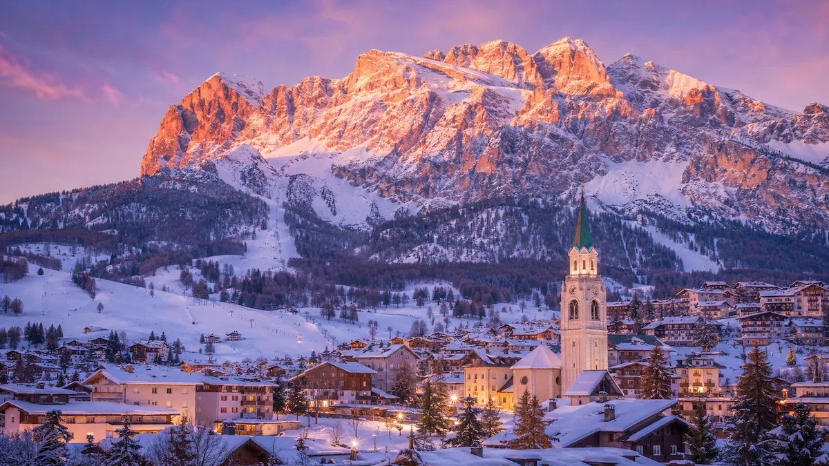Cortina d’Ampezzo nevada al atardecer, con el campanario del pueblo y las montañas Dolomitas iluminadas por el alpenglow.