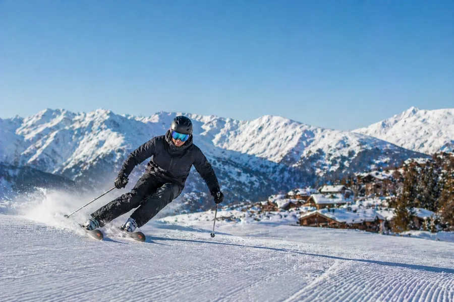 Esquiador tallando curvas con chalets alpinos de fondo en Courchevel