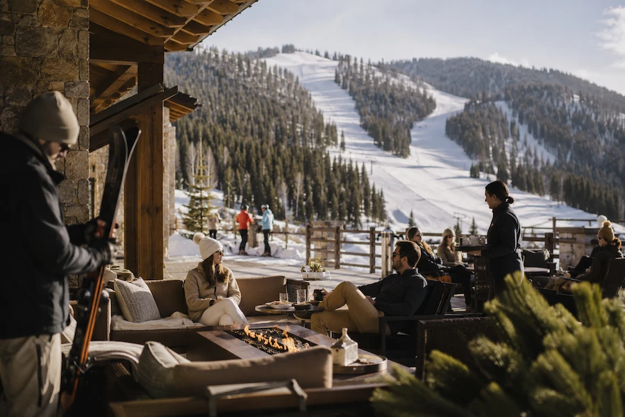 Terraza de resort de esquí en Deer Valley con servicio junto a pistas, chimenea exterior y huéspedes relajados frente a la montaña