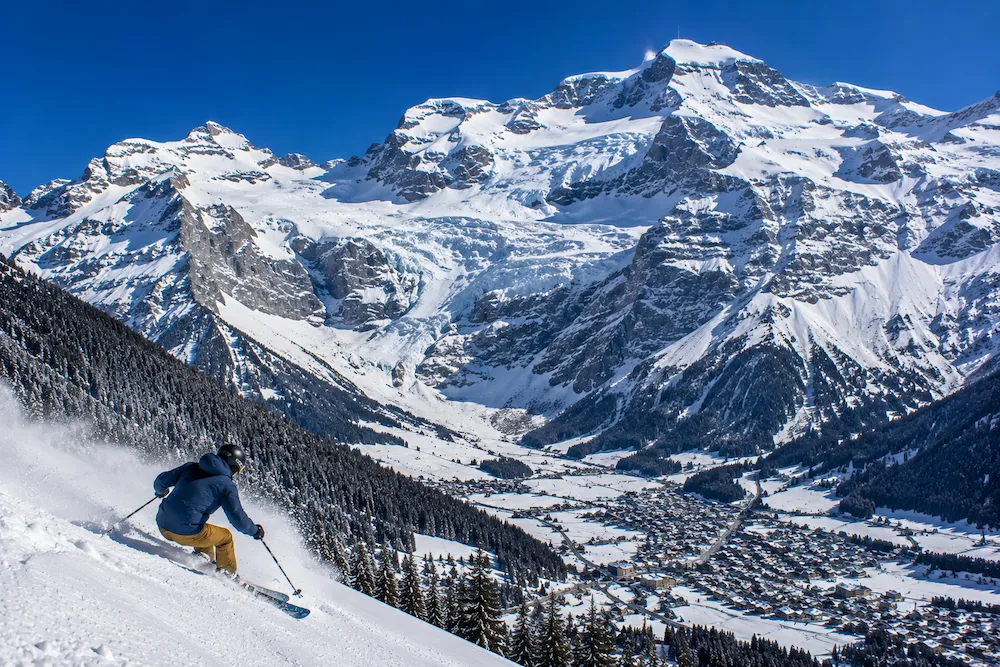 Esquiador descendiendo sobre Engelberg con el glaciar del Titlis dominando el valle suizo bajo cielo azul intenso.