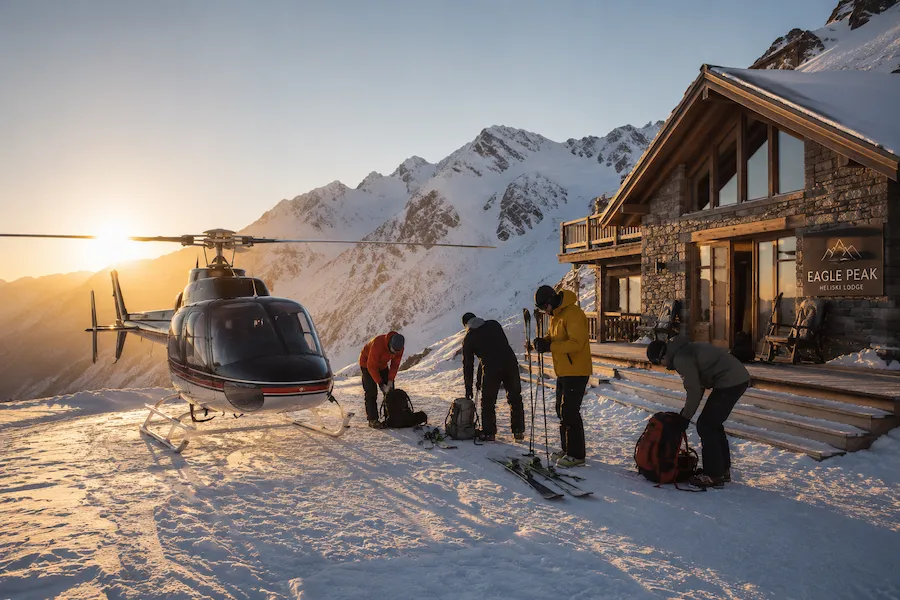Lodge remoto de heliski con helicóptero y esquiadores preparando equipo al amanecer
