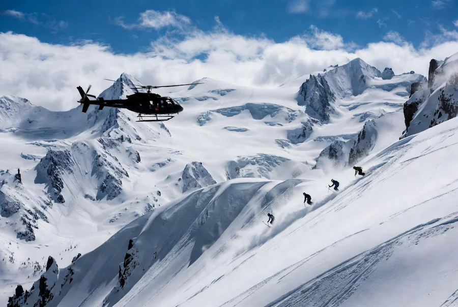 Heliski en alta montaña con helicóptero y esquiadores descendiendo nieve virgen