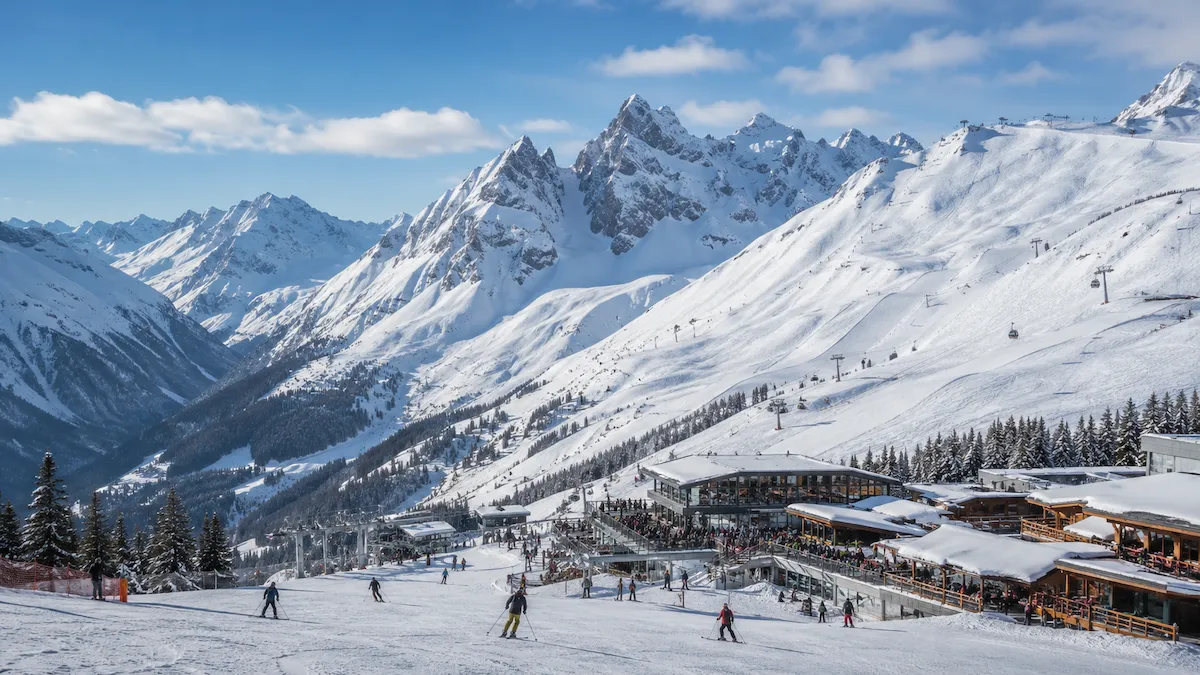 Zona de esquí en Ischgl con pistas soleadas, restaurantes de montaña, remontes y grandes cumbres alpinas al fondo