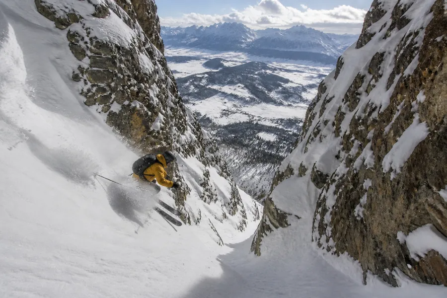 Esquiador descendiendo un couloir empinado en Jackson Hole con nieve profunda y terreno rocoso expuesto