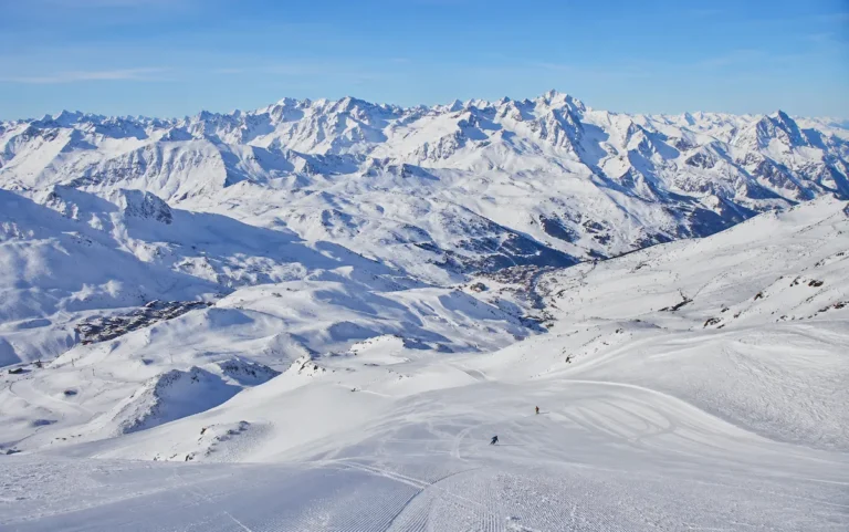 Panorámica nevada de Les 3 Vallées con pistas amplias, esquiadores lejanos y el paisaje alpino entre Courchevel, Méribel y Val Thorens.