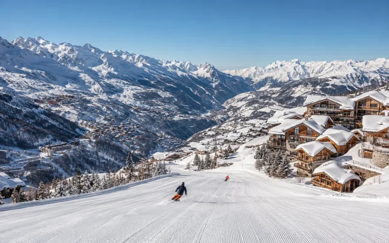 Pista panorámica en Les 3 Vallées con chalets alpinos junto a la nieve y vistas abiertas hacia los valles de Courchevel, Méribel y Val Thorens.