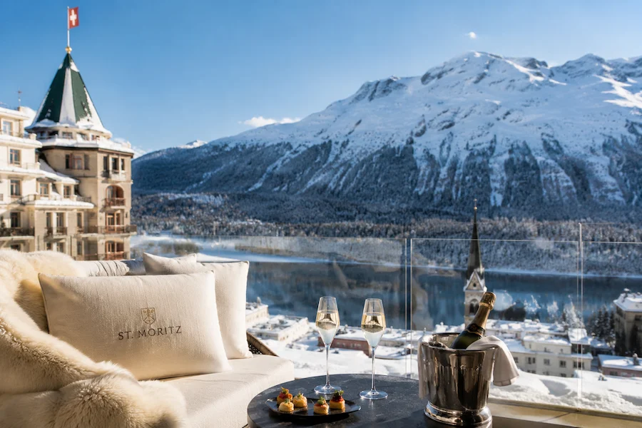 Terraza de lujo en St. Moritz con vistas al lago, montañas nevadas y copas de champagne en un ambiente alpino exclusivo.
