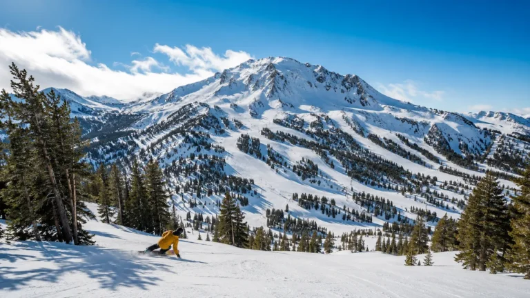 Esquiador descendiendo una ladera amplia en Mammoth Mountain con cielo azul, pinos y montañas nevadas de California
