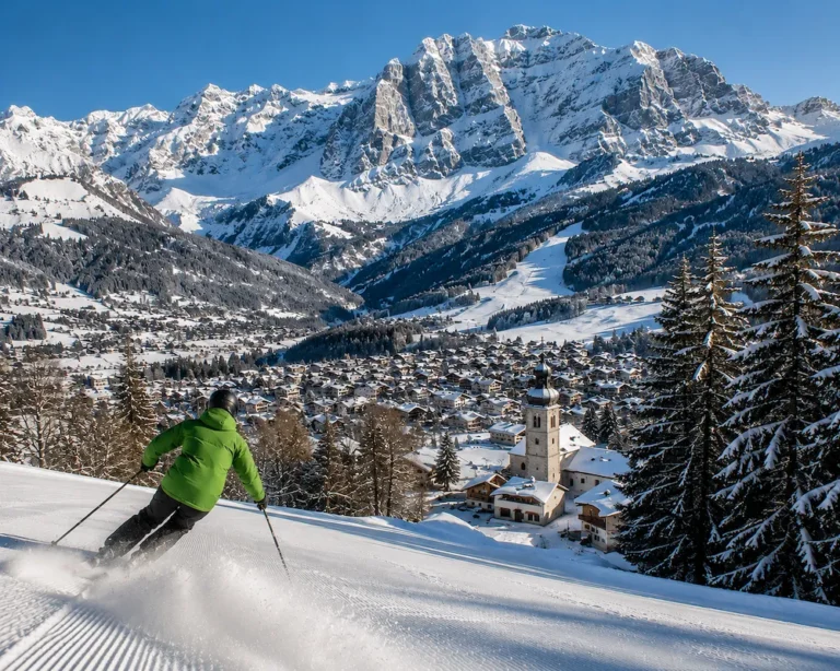 Esquiador con chaqueta verde descendiendo sobre Megève con el pueblo alpino y los Alpes franceses nevados al fondo