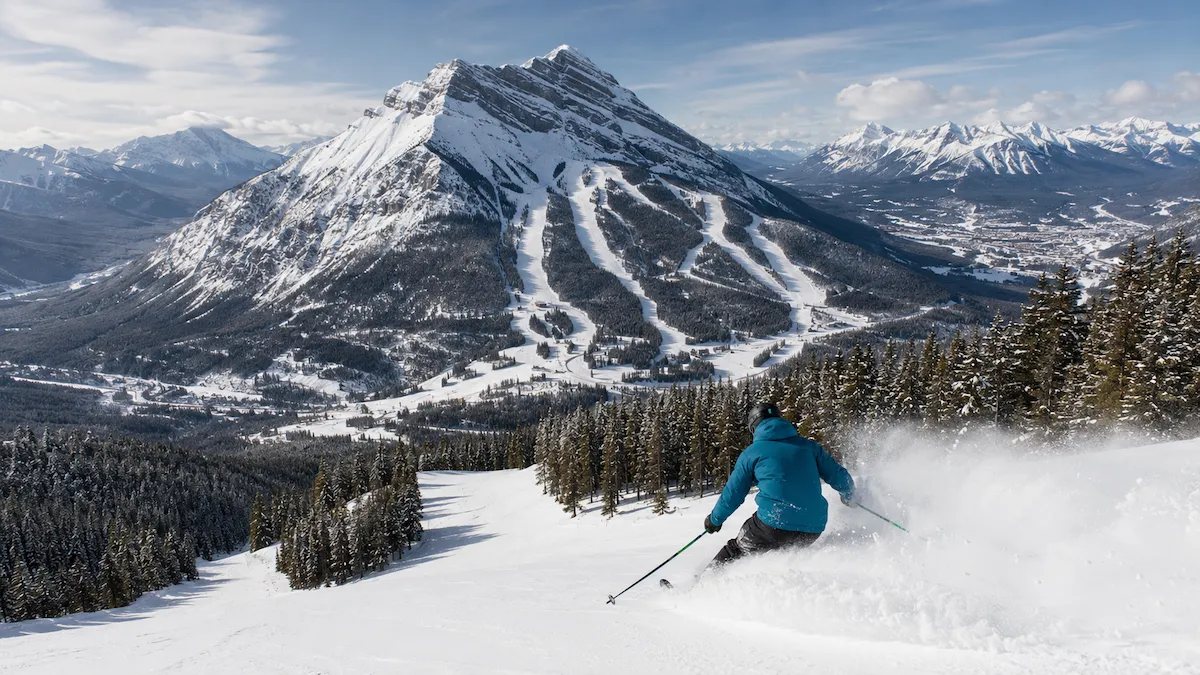 Esquiador descendiendo en Mt. Norquay, con la montaña completa, sus pistas emblemáticas y el valle de Banff al fondo.