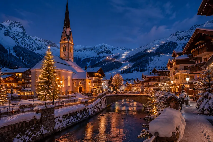Pueblo alpino austríaco iluminado en Navidad con iglesia y montañas nevadas