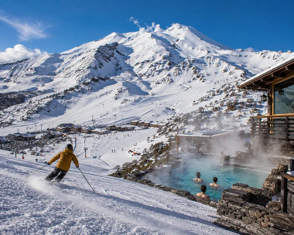Esquiador descendiendo en Nevados de Chillán junto a termas y paisaje volcánico nevado en Chile
