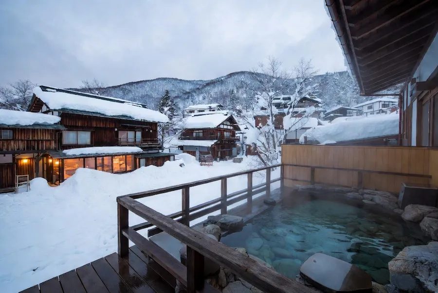 Baño termal exterior en Nozawa Onsen rodeado de nieve y casas tradicionales en Japón