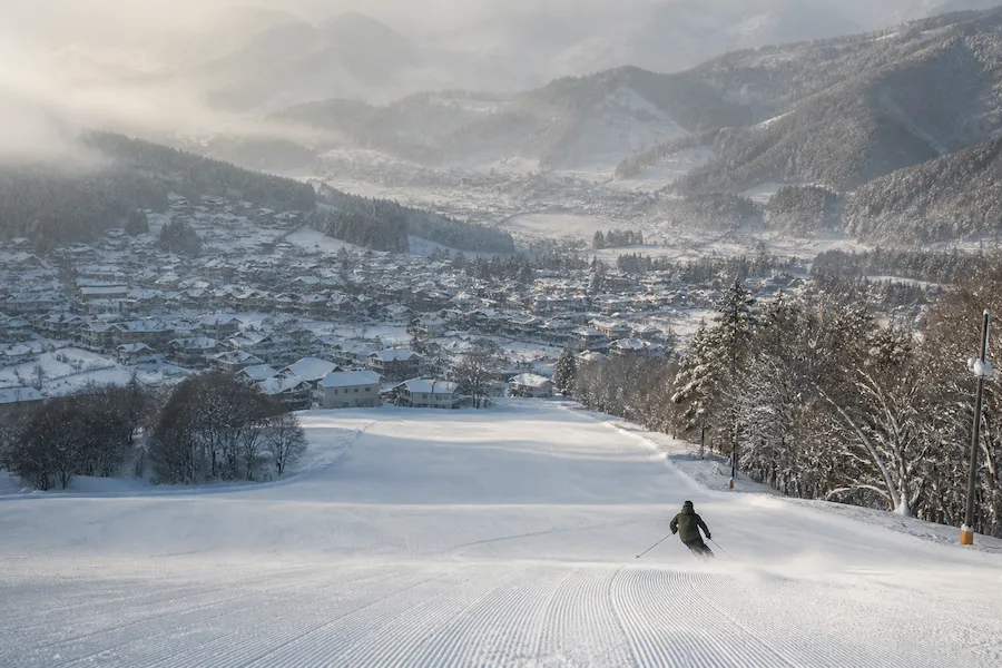 Esquiador descendiendo con vistas al pueblo de Nozawa Onsen en Nagano, Japón