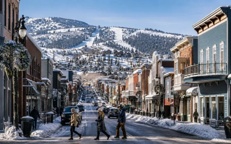 Calle principal de Park City cubierta de nieve, con edificios históricos, ambiente urbano alpino y pistas de esquí al fondo.