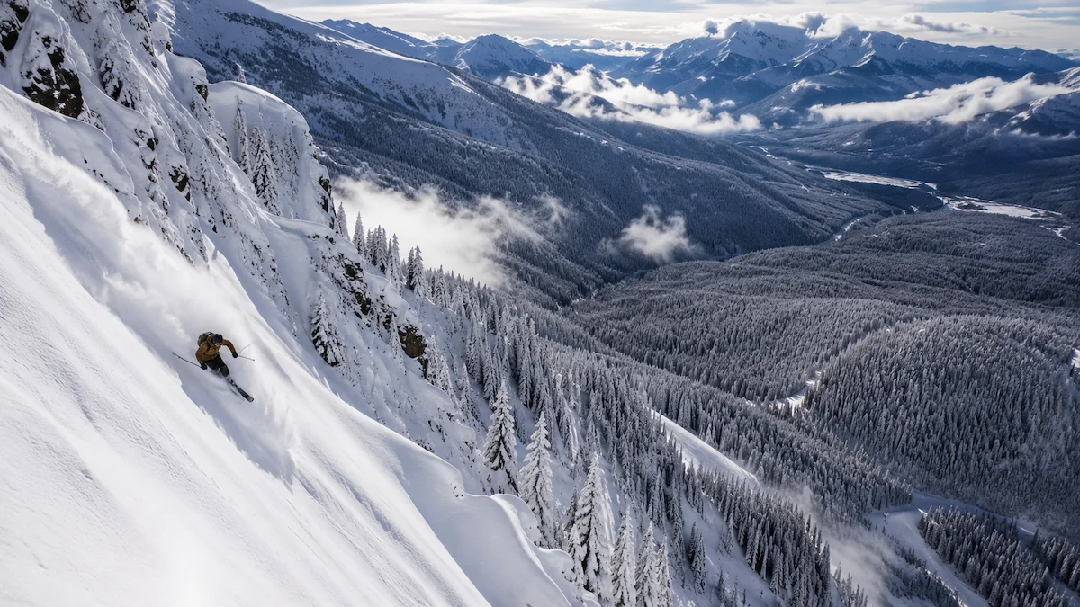 Esquiador descendiendo una ladera empinada sobre un inmenso valle boscoso nevado en Revelstoke