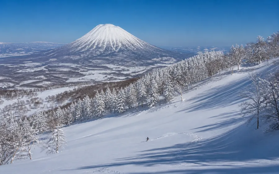 Esquiador descendiendo con el monte Yotei al fondo en Rusutsu, Hokkaido, Japón