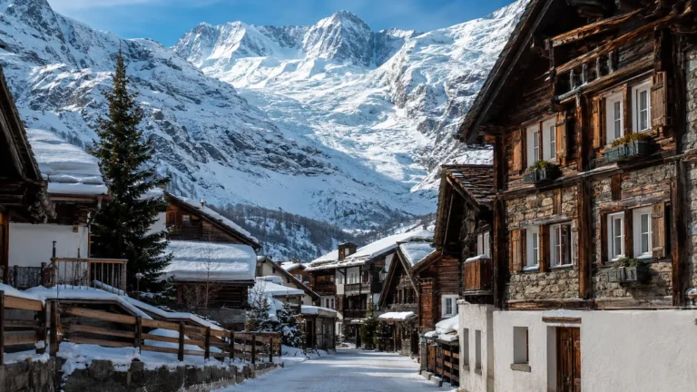 Calle nevada de Saas-Fee con chalets alpinos de madera y un gran glaciar suizo al fondo