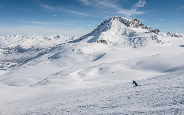 Vista panorámica de Tignes en torno al glaciar de Grande Motte, con amplias laderas nevadas de alta altitud y un esquiador descendiendo bajo luz natural.