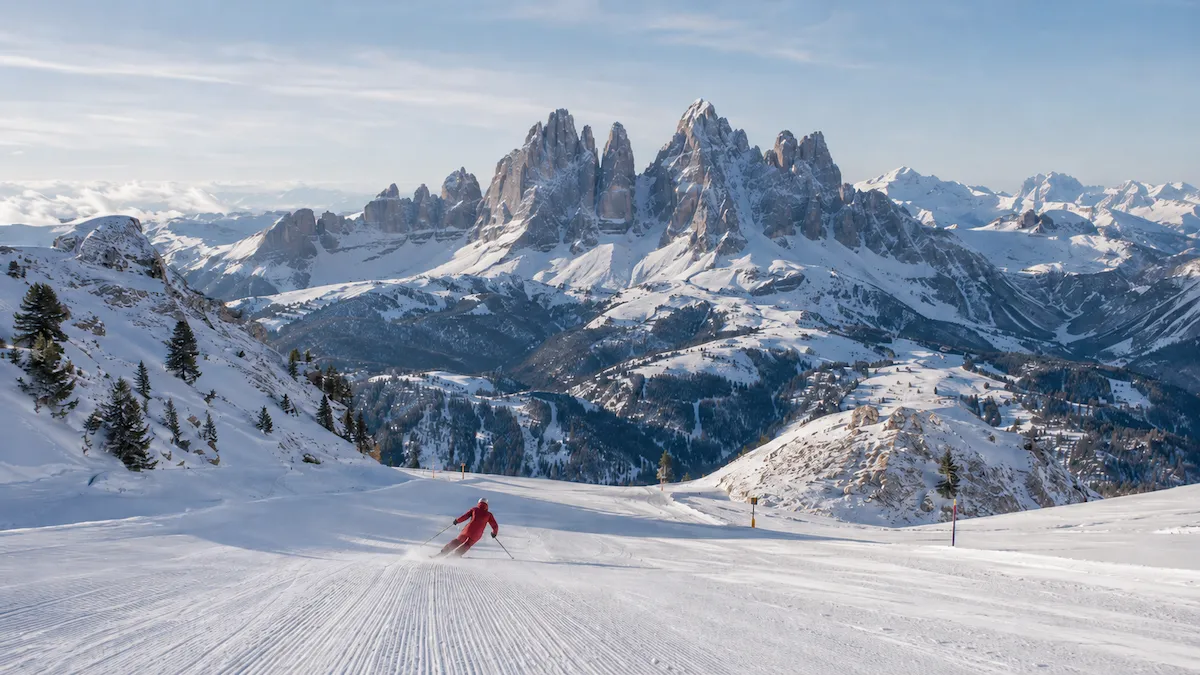 Esquiador descendiendo en Val Gardena desde la zona de Seceda, con las agujas Odle/Geisler y los Dolomitas al fondo.