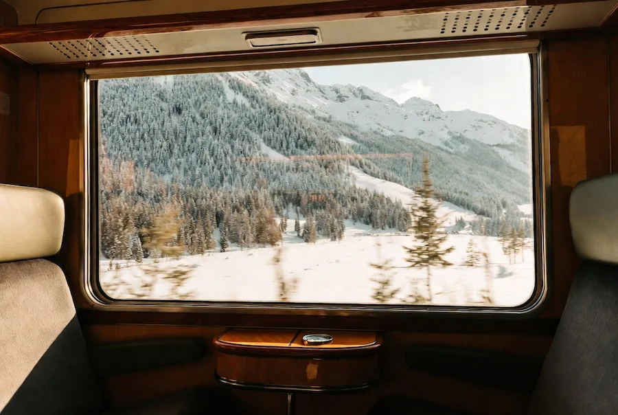 Interior de un tren alpino con ventana panorámica y paisaje nevado de montaña al fondo
