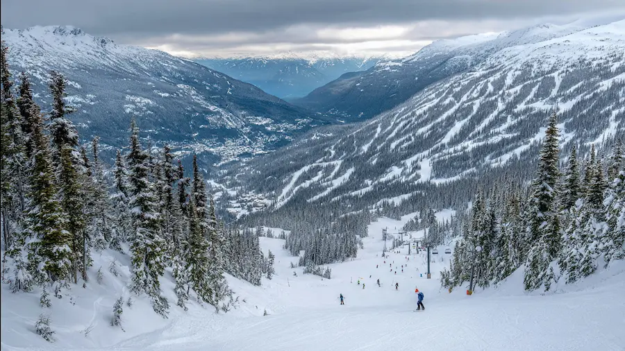 Esquiadores descendiendo una pista amplia en Whistler con terreno fluido y vistas al valle